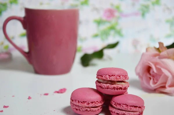 Three pink almond macaroons and mug with coffee on a white wooden background next to a pale pink rose. good morning concept — Stock Photo, Image