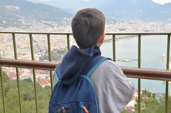Küçük çocuk, Akdeniz körfezinin muhteşem manzarasına bakıyor. Turistik gemileri, süslü şatosu ve sırtında sırt çantası olan dağdan bir şehir..