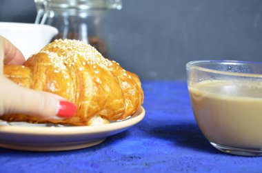 Bir tabak kruvasan ve sütlü kahve. Üst Manzara. Kruvasan susamla süslenmiş. Kahve çekirdeği ve süt sürahisinin bileşimini tamamla. Sağlıklı kahvaltı. Günaydın.