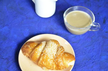 Bir tabak kruvasan ve sütlü kahve. Üst Manzara. Kruvasan susamla süslenmiş. Kahve çekirdeği ve süt sürahisinin bileşimini tamamla. Sağlıklı kahvaltı. Günaydın.