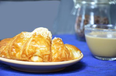 Bir tabak kruvasan ve sütlü kahve. Üst Manzara. Kruvasan susamla süslenmiş. Kahve çekirdeği ve süt sürahisinin bileşimini tamamla. Sağlıklı kahvaltı. Günaydın.