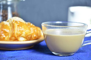 Bir tabak kruvasan ve sütlü kahve. Üst Manzara. Kruvasan susamla süslenmiş. Kahve çekirdeği ve süt sürahisinin bileşimini tamamla. Sağlıklı kahvaltı. Günaydın.