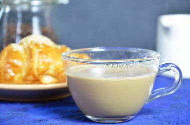 Bir tabak kruvasan ve sütlü kahve. Üst Manzara. Kruvasan susamla süslenmiş. Kahve çekirdeği ve süt sürahisinin bileşimini tamamla. Sağlıklı kahvaltı. Günaydın.