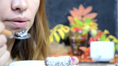 Bir kız sonbaharda lezzetli bir çikolatalı kek yer ve bir kafede kahve içer, sarı ve kırmızı sonbahar yapraklarının arka planında. Genç ve güzel bir kadın tatlı yiyor.