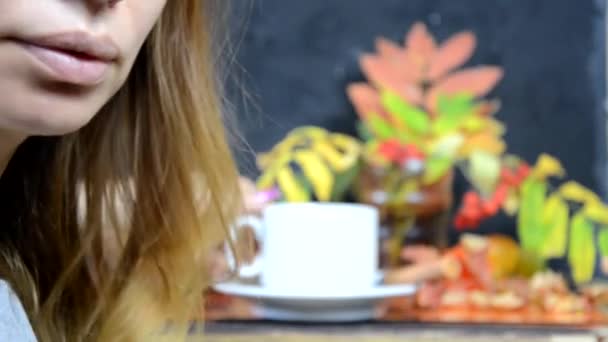 한 소녀는 맛있는 초콜릿 케이크를 먹고, 가을에는 카페에서 노란색과 빨간색의 단풍 잎을 배경으로 커피를 마십니다. 아름다운 여인이 디저트를 먹고 있다 — 비디오
