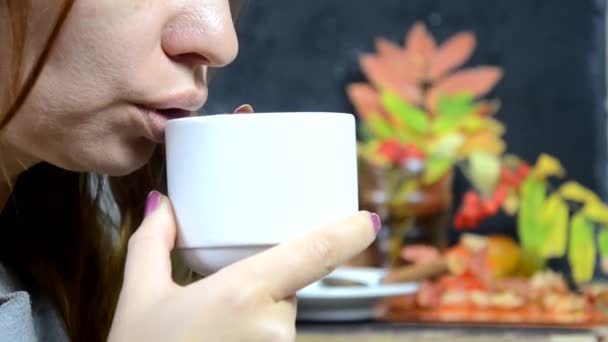 Dziewczyna je pyszne ciasto czekoladowe i pije kawę w kawiarni jesienią, na tle żółtych i czerwonych jesiennych liści. młoda piękna kobieta jedząca deser — Wideo stockowe