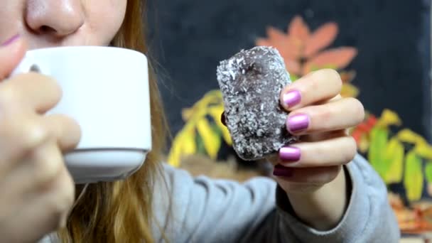 Девушка ест вкусный шоколадный торт и пьет кофе в кафе осенью, на фоне желтых и красных осенних листьев. молодая красивая женщина ест десерт — стоковое видео