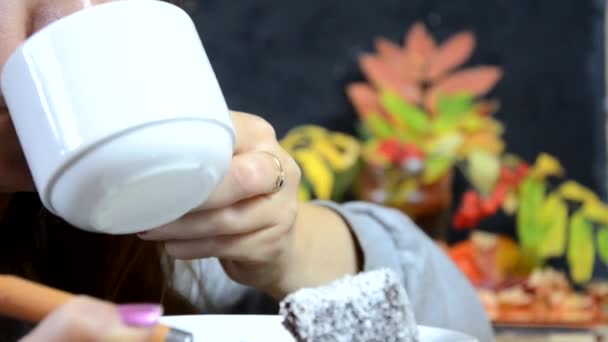 Ein Mädchen isst im Herbst vor dem Hintergrund gelb-roter Herbstblätter einen leckeren Schokoladenkuchen und trinkt Kaffee in einem Café. junge schöne Frau isst ein Dessert