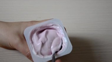 Plastik bir kavanozdan bir çay kaşığı pembe yoğurt yiyen bir kız. Sağlıklı beslenme, vejetaryen yiyecekler, diyet ve insan konsepti - masada yoğurt ve böğürtlen ile kadın ellerine yakın çekim