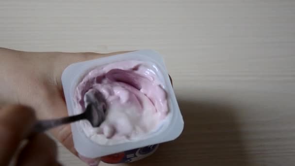 Ragazza che mangia un cucchiaino di yogurt rosa da un barattolo di plastica. alimentazione sana, cibo vegetariano, dieta e concetto di persone - primo piano delle mani della donna con yogurt e bacche sul tavolo — Video Stock