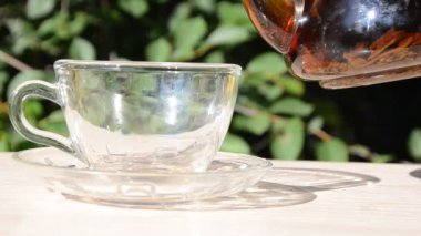 Bir kız şeffaf bir çaydanlıktan şeffaf bir fincana yeşil yapraklı bir fincana çay dolduruyor. Günaydın, açık kafe, enerji takviyesi. Çayın içine çay dökülüyor.