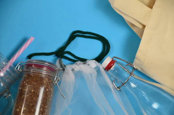 Plastiksiz, sıfır atık alışverişi ve yaşam. Yeniden kullanılabilir, geri dönüştürülmüş, meyve ve sebzeler için ev yapımı ürün torbası, tekstil torbası, paslanmaz çelik şişe, mavi üzerine cam bir kavanoz..