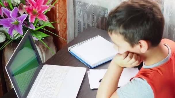 Ragazzo studia a casa al computer. istruzione remota, il bambino della scuola impara lezioni online utilizzando la trasmissione video e le tecnologie moderne, guarda lo schermo del monitor e fa i compiti, imparando online — Video Stock