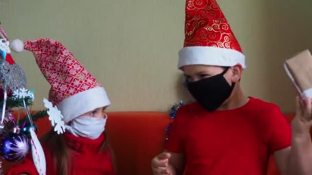 Dívka a chlapec v masce, vánoční koronavirus a pandemický koncept, bratr a sestra vybalují dárky, novoroční koncept, rodina — Stock video