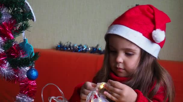 Glückliches kleines Mädchen schmückt den Weihnachtsbaum mit schönen Ornamenten und Kugeln und genießt die festliche Dekoration zu Hause an einem ruhigen Winterabend 4k Filmmaterial — Stockvideo