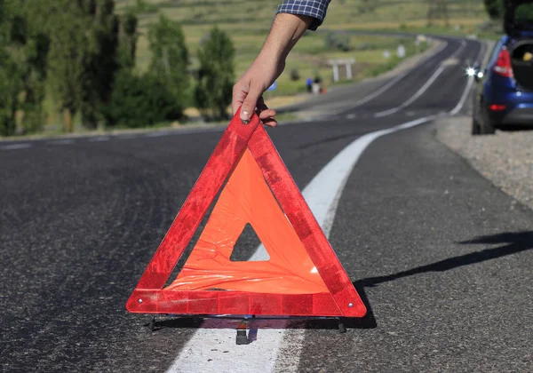 A man is putting on the road Danger Safety Warning Triangle Sign. Triangular safety alert sign holds in hand. Road accident