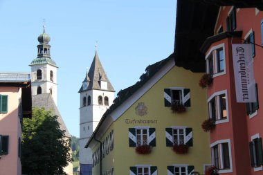 KITZBUEHEL, AUSTRIA - 8 Ağustos 2025: Eski Kitzbuehel kasabasındaki renkli tarihi binalar ve kilise manzarası. Yüksek kalite fotoğraf