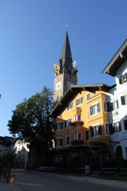 KITZBUEHEL, AUSTRIA - 8 Ağustos 2025: Tarihi Kitzbuehel kasabasında saat ve renkli evlere sahip kilise kulesi manzarası. Yüksek kalite fotoğraf