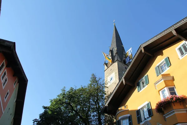 KITZBUEHEL, AUSTRIA - 8 Ağustos 2025: Eski Kitzbuehel kasabasında renkli evleri olan tarihi kilise kulesinin manzarası. Yüksek kalite fotoğraf