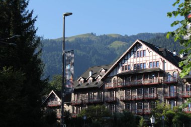KITZBUEHEL, AUSTRIA - AUGUST 8, 2025: Traditional alpine hotel with wooden balconies and mountain backdrop on a sunny day. High quality photo