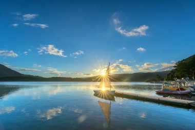 Gökyüzünden güzel günbatımında güneş yıldız ile yalnız Yelkenli parlar ve göl yüzeyine onları izlerken sakin ve huzurlu