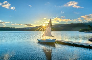 Gökyüzünden güzel günbatımında güneş yıldız ile yalnız Yelkenli parlar ve göl yüzeyine onları izlerken sakin ve huzurlu