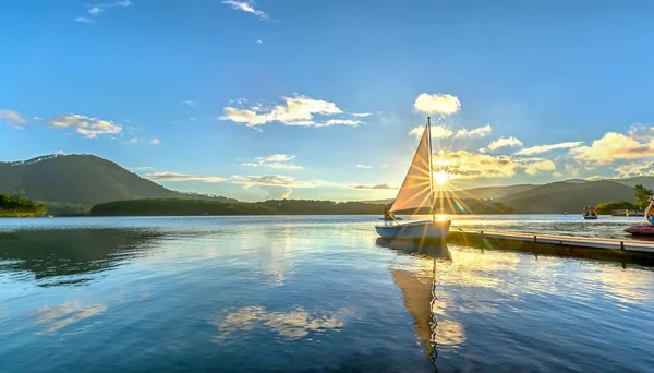 Gökyüzünden güzel günbatımında güneş yıldız ile yalnız Yelkenli parlar ve göl yüzeyine onları izlerken sakin ve huzurlu