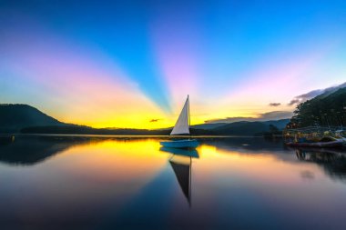 Göl güneş ile güzel gün batımı sırasında yalnız Yelkenli bulutlar parlar gökten gün sonuna mistik gölden yansıtan renkli ışınları