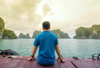 Adalar arasında Vietnam'da Halong Körfezi'ne bakan teknede geri görünüm adam gezgin.