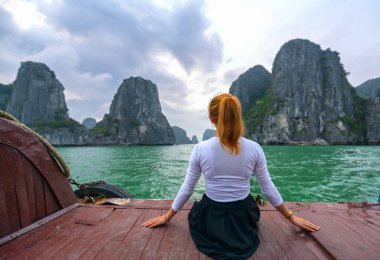Back view kadın gezgin Halong Bay, Vietnam adalar arasında rahat görünümlü teknede oturan.