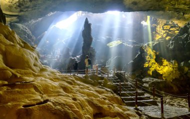 Silhouette visitors conquering Sung Sot cave beautiful view of sunrays shining through cave in Ha Long bay, Vietnam clipart