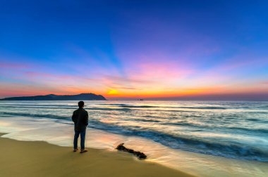 Plaj büyülü dramatik gündoğumu görünümlü adam silüeti. Kumlu plajda duran adam