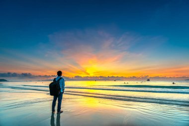 Sahilde adam backpacker siluet büyülü dramatik gündoğumu bakarak. Kumsalda duran adam.