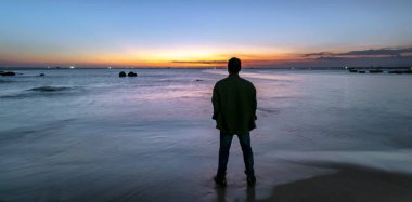 Siluet gezgin adam denizin önünde gün batımını izlerken ayakta