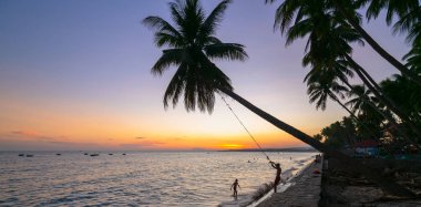 Güzel plajda bir hindistan cevizi ağacı banyo ve gün batımı üzerinde sallanan çocukların silueti