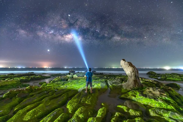 夜景与乳白色的方式和剪影的一个快乐的男人站在沙滩上的青苔岩石旁边 — 图库照片