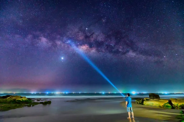 夜景与乳白色的方式和剪影的一个快乐的男人站在沙滩上的青苔岩石旁边 — 图库照片