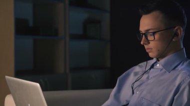 Karanlık bir ofiste bir dizüstü bilgisayar, bir adam oturuyor. Adam geç saatlere kadar çalışıyor