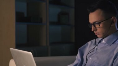 Karanlık bir ofiste bir dizüstü bilgisayar, bir adam oturuyor. Adam geç saatlere kadar çalışıyor