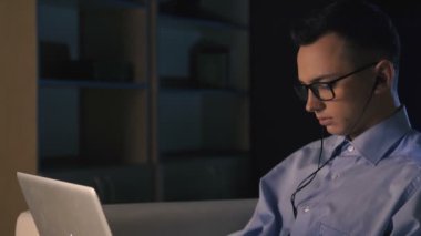 Karanlık bir ofiste bir dizüstü bilgisayar, bir adam oturuyor. Adam geç saatlere kadar çalışıyor