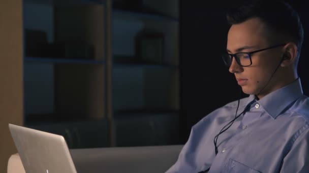 Un homme est assis à un ordinateur portable dans un bureau sombre. Il travaille tard. — Video