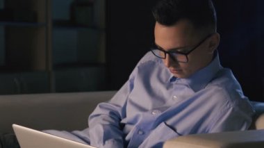 Karanlık bir ofiste bir dizüstü bilgisayar, bir adam oturuyor. Adam geç saatlere kadar çalışıyor