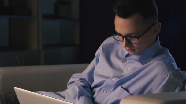 En mand sidder på en bærbar computer på et mørkt kontor. Manden arbejder til sent. – Stock-video
