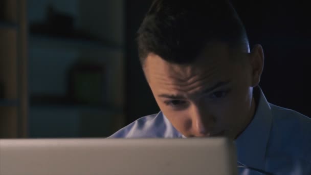 Ein Mann sitzt an einem Laptop in einem dunklen Büro. arbeitet bis spät, Anpassungsschwierigkeiten bei der Arbeit — Stockvideo