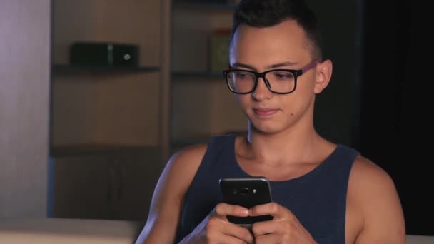 Un joven con gafas rosas reescribe emocionalmente por teléfono, sobre un fondo oscuro . — Vídeos de Stock