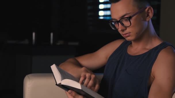 Un étudiant lit un livre après une journée bien remplie, assis sur un lit . — Video