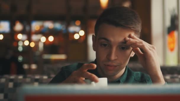 Ein junger Geschäftsmann sitzt an einem Tisch in einem Café, blickt in einen Laptop und beobachtet Passanten. Erfolgreiche Menschen, tägliche Routine. Unterhaltsam, entspannend, plaudernd. — Stockvideo