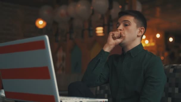 Un joven empresario está sentado en una mesa en un café, mirando un portátil y mirando a los transeúntes. Gente exitosa, rutina diaria. Entretenido, relajante, charlando . — Vídeos de Stock