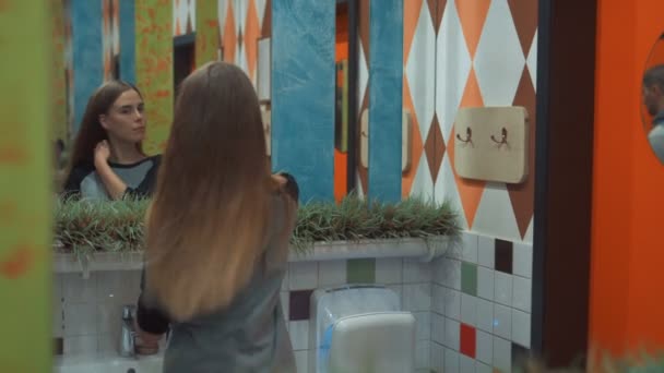 Ein junges Mädchen in schwarzer Kleidung betrachtet ihr Spiegelbild im Spiegel und kämmt ihre langen Haare. manuelle Nahaufnahme in Echtzeit — Stockvideo