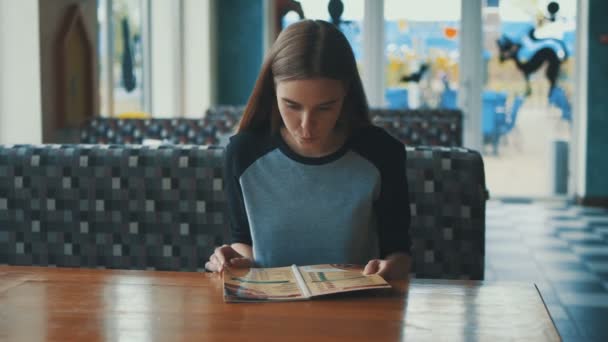 Девушка изучает меню в кафе замедленной съемки. Девушка ждет фаст-фуд. Компания друзей, которые едят в кафе. концепция быстрого питания для девочек — стоковое видео